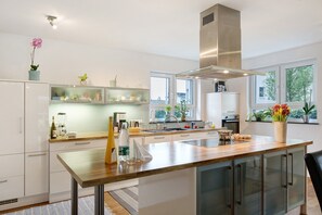 Une cuisine moderne avec des armoires blanches, un îlot central en bois et une hotte de cuisine en acier inoxydable.