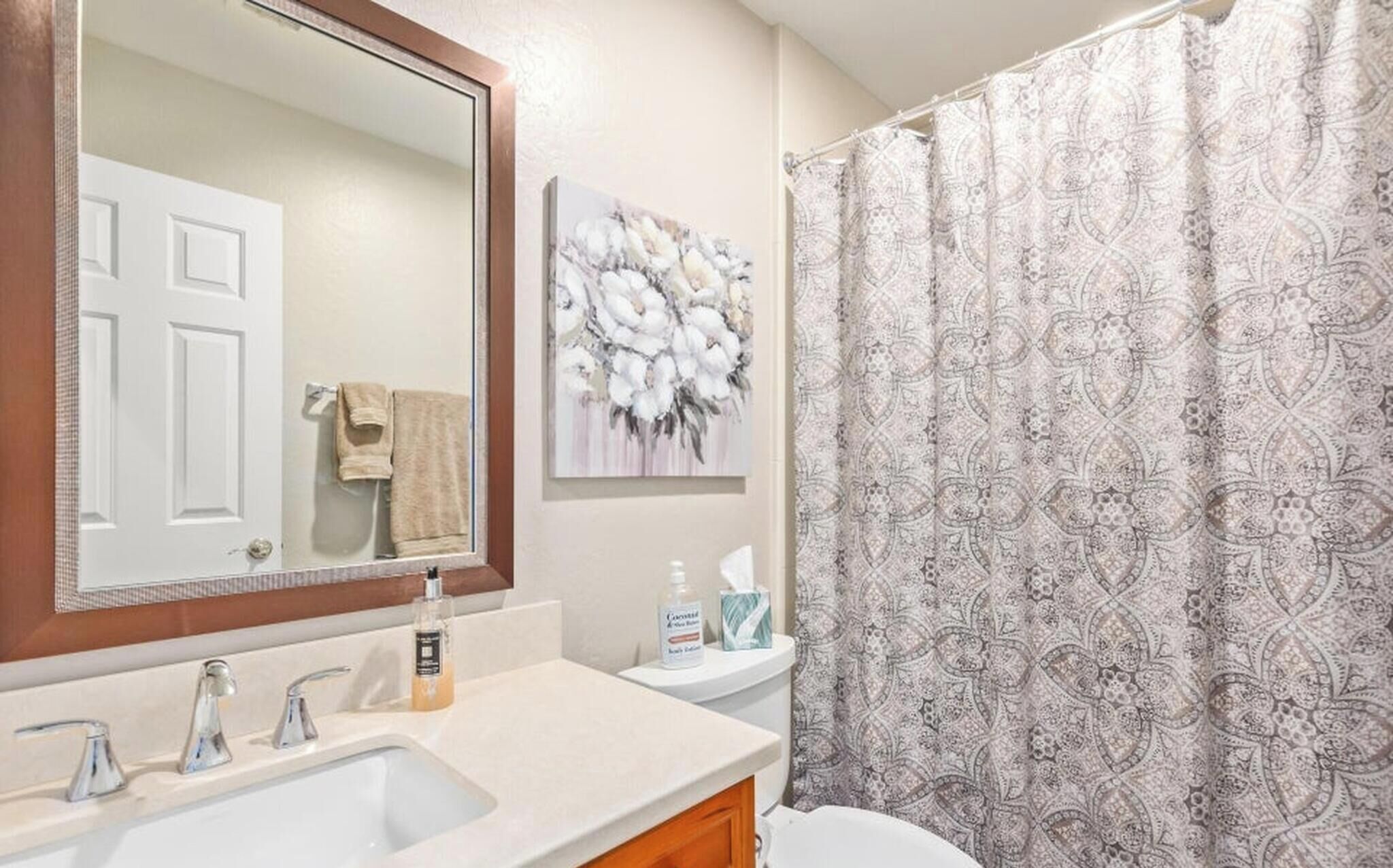 A bathroom with a sink, mirror, toilet, and shower curtain.