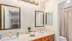 Ein Badezimmer mit zwei Waschbecken, Holzschränken, einem Spiegel und einer Duschvorhang.