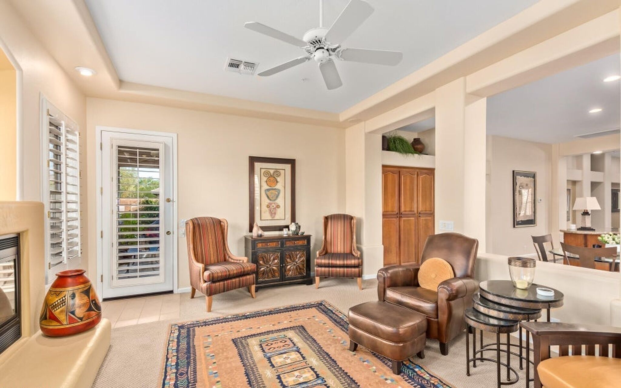 A living room with a ceiling fan, a fireplace, a patterned rug, and a dining area with a table and chairs.