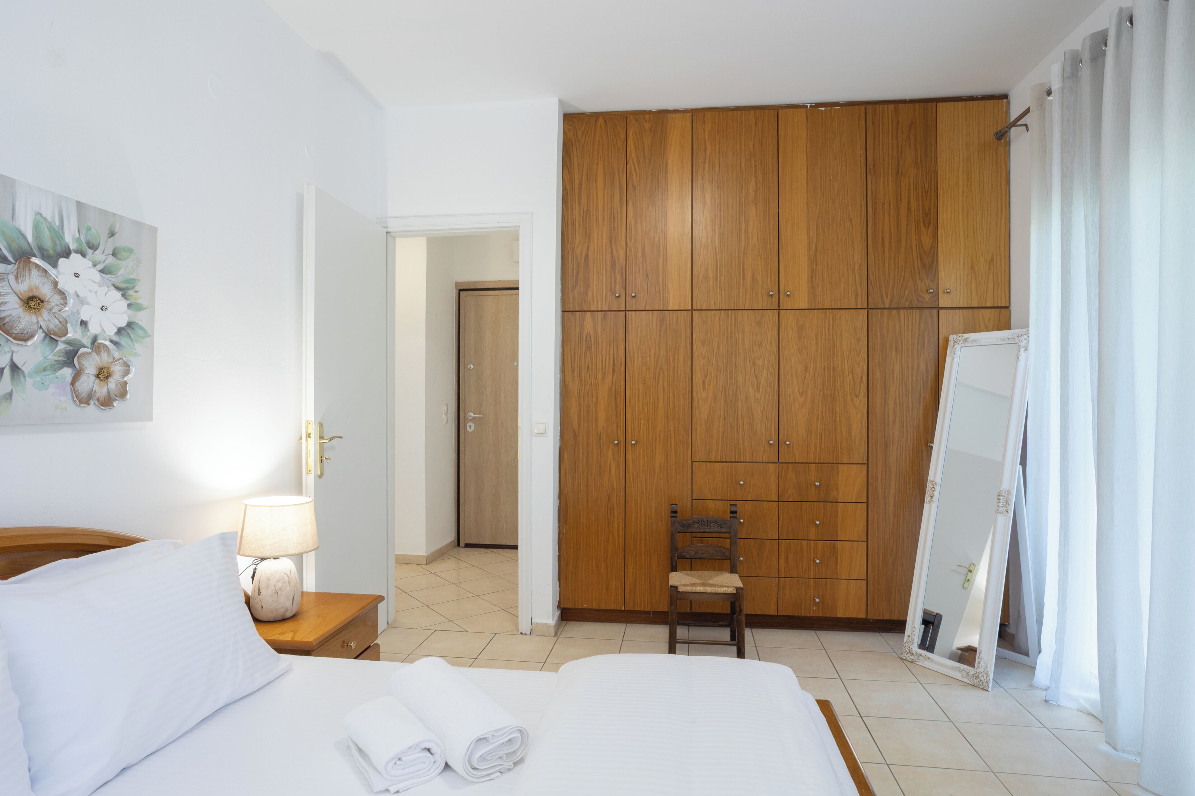 A hotel room with a bed, a chair, a wardrobe, a mirror, and a painting on the wall.