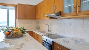 A kitchen with wooden cabinets, a stainless steel oven, a marble countertop, and a view through a sliding glass door.
