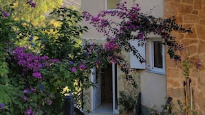 A modern building with a stone facade, a balcony with purple flowers, and a clear sky.