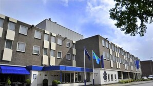 Ein mehrgeschossiges Hotel mit schlichter Fassade, einer überdachten Eingangsseite und Flaggen.