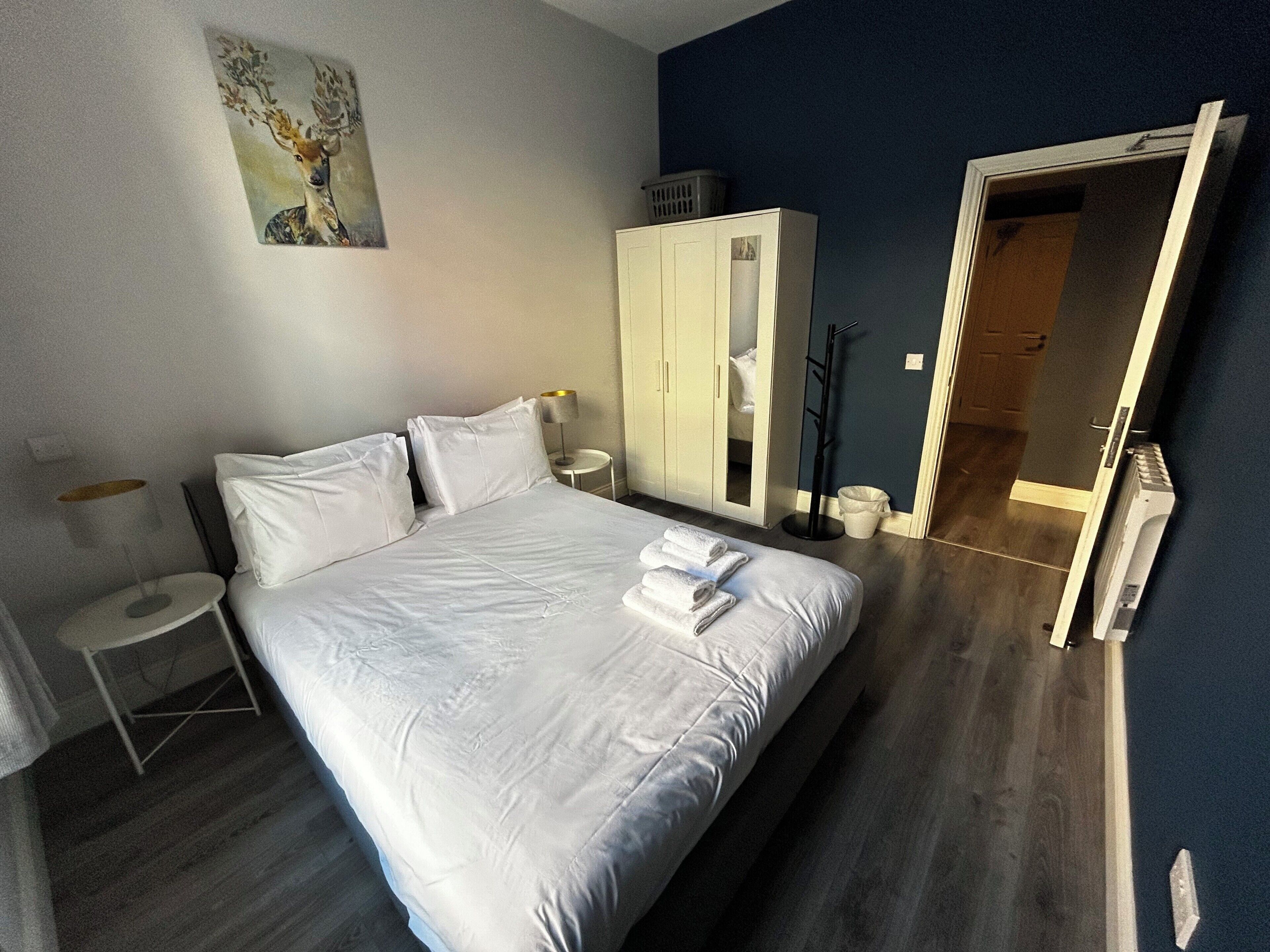 Une chambre d’hôtel avec un lit, une armoire, un miroir, une petite table et une lampe.