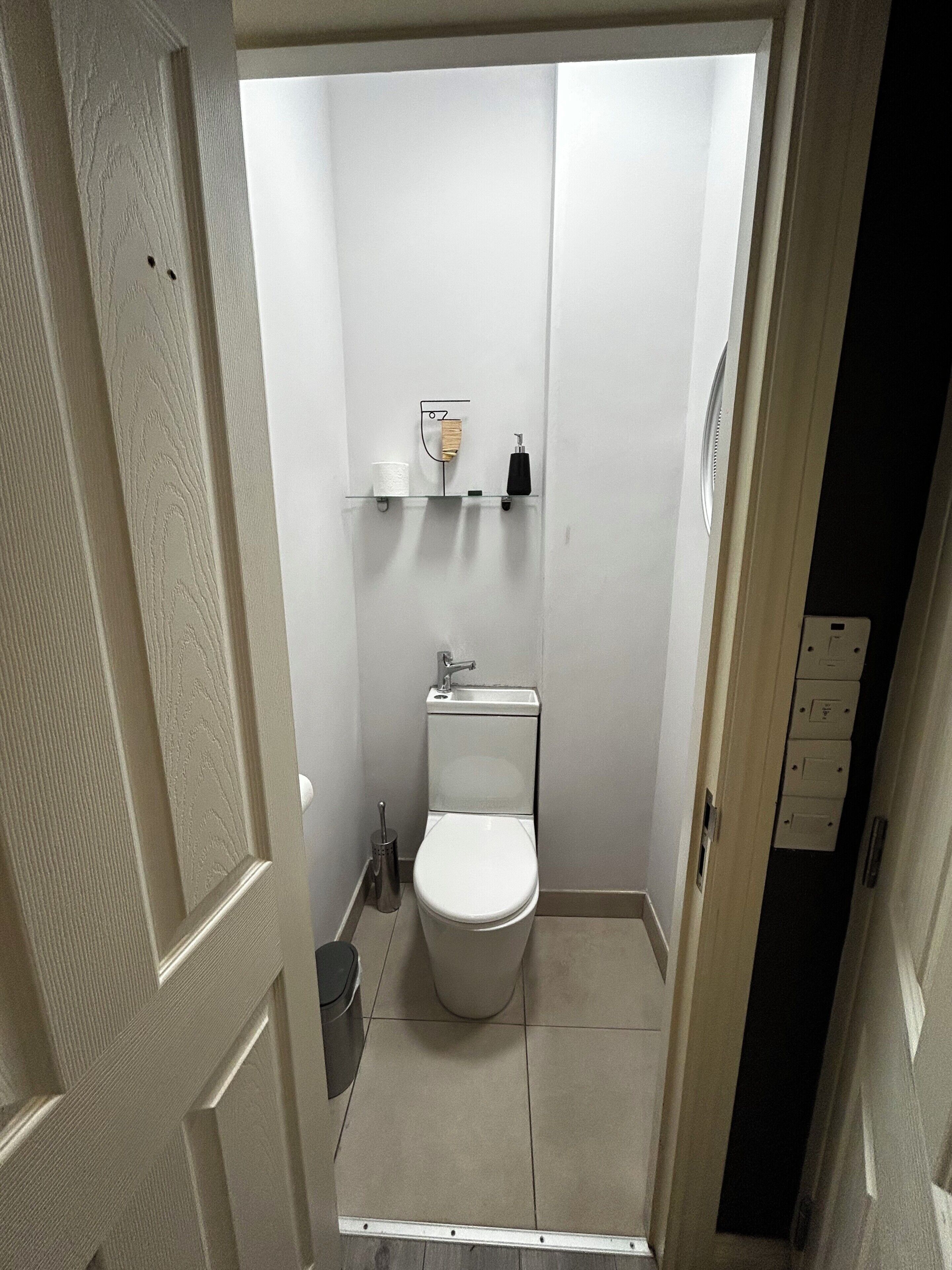 Een kleine, smalle badkamer met een toilet, een plankje met een tandenborstel en een handdroger.