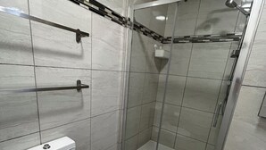Kylpyhuone, jossa on wc, lasiseinällä varustettu suihku ja laatoitetut seinät.