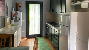 A kitchen with a dining area, a window with curtains, and a door. - Sardinia Hillside Retreat - Apt 13 - 2BR, quiet area, parking (Santa Maria Coghinas)