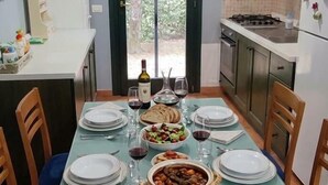 Un comedor con una mesa dispuesta para cuatro personas, una cocina al fondo y vistas a través de un ventanal.