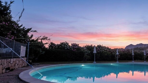 A swimming pool with a sunset view, a stone wall, and a building with a red roof. - Sardinia Hillside Retreat - Apt 13 - 2BR, quiet area, parking (Santa Maria Coghinas)