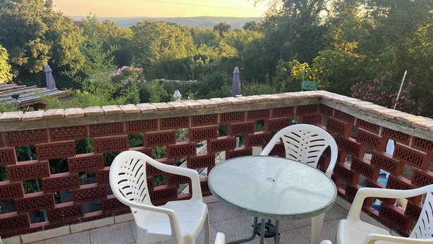 Eine Terrasse mit einem runden Tisch und vier weißen Plastikstühlen, umgeben von einer Ziegelmauer mit Gitterwerk.