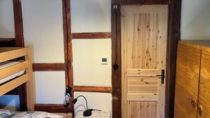 Ein Zimmer mit sichtbaren Holzbalken, einem Etagenbett, einem Schreibtisch mit Lampe, einem Kleiderschrank und einer Tür mit Griff.
