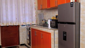 Una cocina con refrigerador, horno, microondas y armarios color naranja.