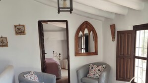 Una sala de estar con un sofá gris, un tapete estampado, una puerta de madera y una pequeña mesa con una lámpara.