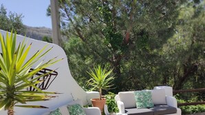 Un espacio al aire libre con sofás blancos, cojines de estampado verde y una mesa de madera.