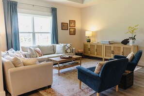 Un soggiorno con divano, poltrone, tavolino, credenza e lampada.