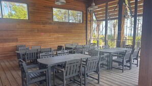 A wooden deck with tables and chairs, large windows, and a view of trees.