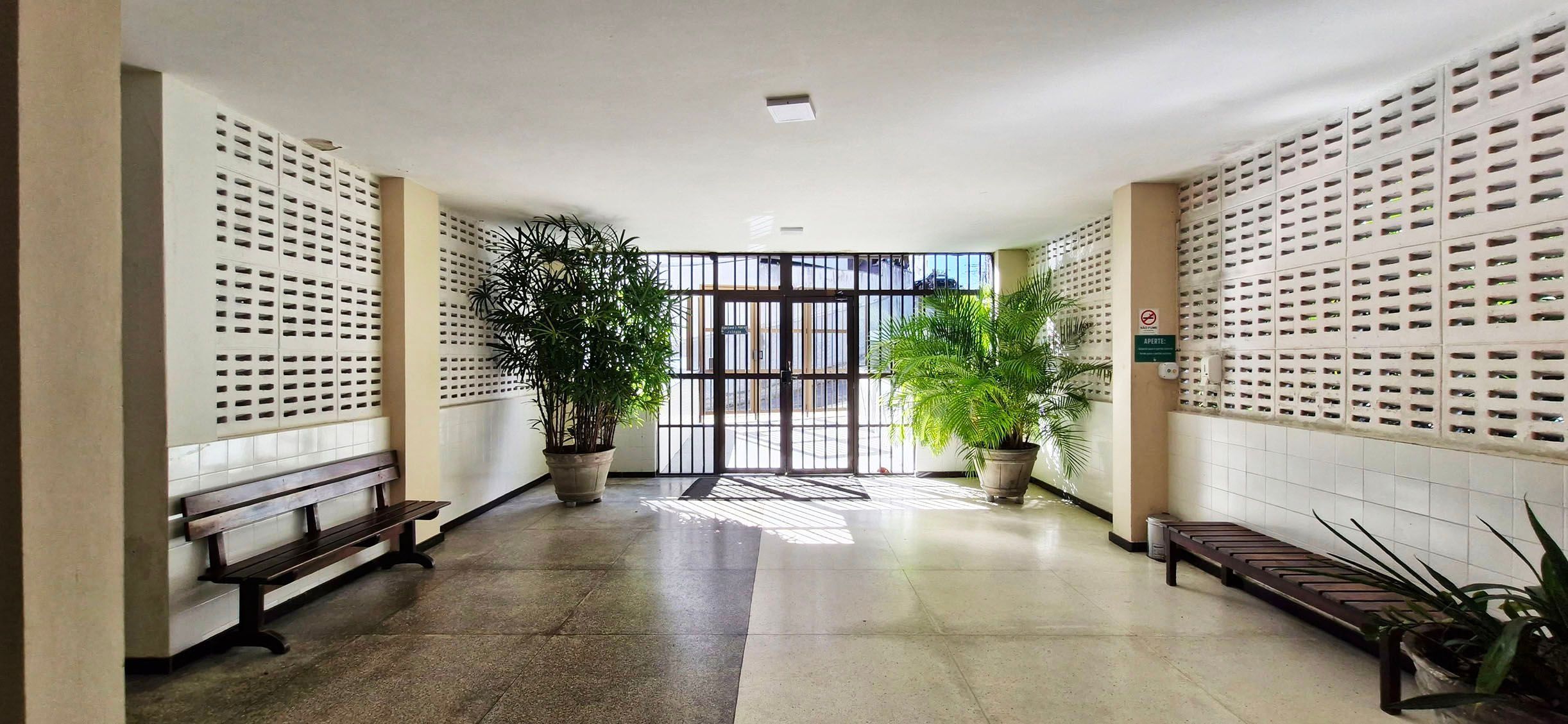 A hallway with a bench, potted plants, and a door with a metal gate.
