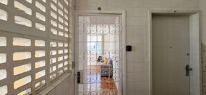 Un pasillo con una puerta blanca, una reja metálica y vistas a una habitación con un sofá y una silla.