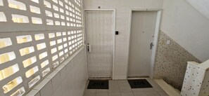 A narrow hallway with a white door, a barred window, and a tiled wall with a pattern. - COGRA0105 - Edificio Jaragua (Salvador)
