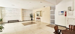 A spacious lobby with a bench, a potted plant, a small table, and a fire extinguisher. - COGRA0105 - Edificio Jaragua (Salvador)