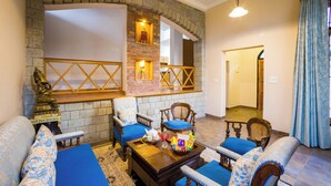 A living room with a brick fireplace, blue upholstered furniture, and a wooden coffee table with decorative items. - Alaya Stays Mehar Villa 3BHK With Garden (Kasauli)