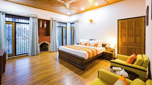 A bedroom with a wooden ceiling, a bed with orange and white bedding, a green sofa, a fireplace, and a wooden door. - Alaya Stays Mehar Villa 3BHK With Garden (Kasauli)