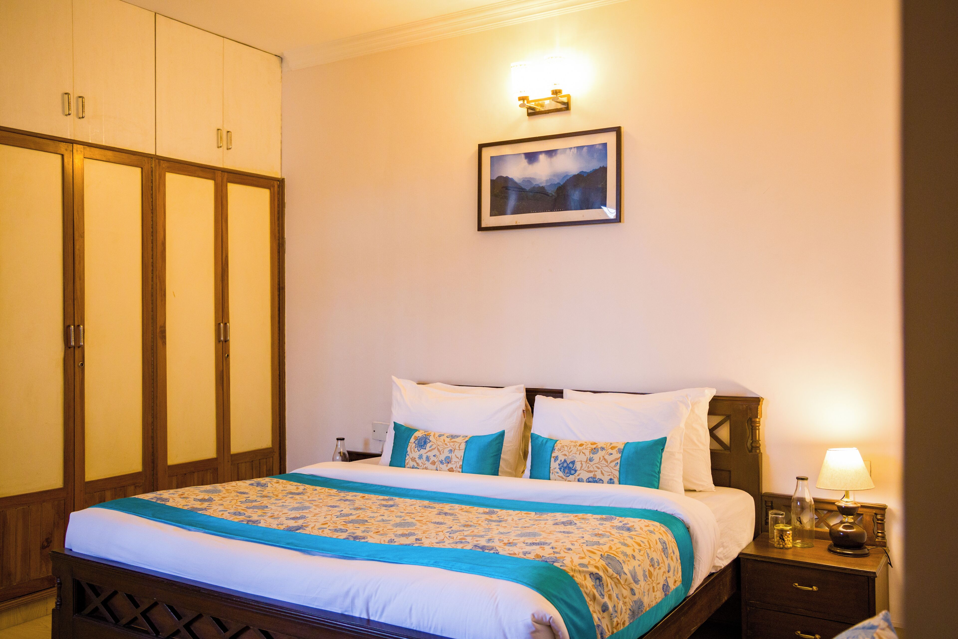 A hotel room with a bed, a nightstand, a lamp, a framed picture on the wall, and a wardrobe.