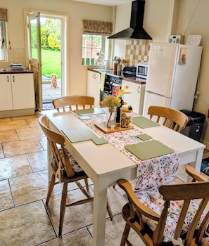 A kitchen with a dining table, chairs, a stove, a microwave, and a refrigerator. - Beaconsfield Cottage (Melton Constable)