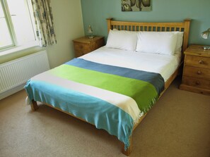 A neatly made bed with a striped bedspread, a wooden headboard, and two bedside tables with lamps. - Beaconsfield Cottage (Melton Constable)