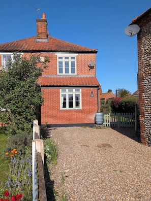 A two-story brick house with a red-tiled roof, a gravel driveway, and a white picket fence. - Beaconsfield Cottage (Melton Constable)