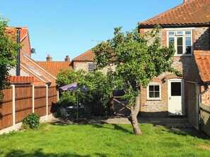 A residential backyard with a patio, a tree, and a brick house. - Beaconsfield Cottage (Melton Constable)