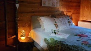 A wooden cabin room with a bed, a small table with a lamp, and a wall decorated with floral prints. - Brechts Boshuisje Quiet Holiday Home with Sauna (Brecht)