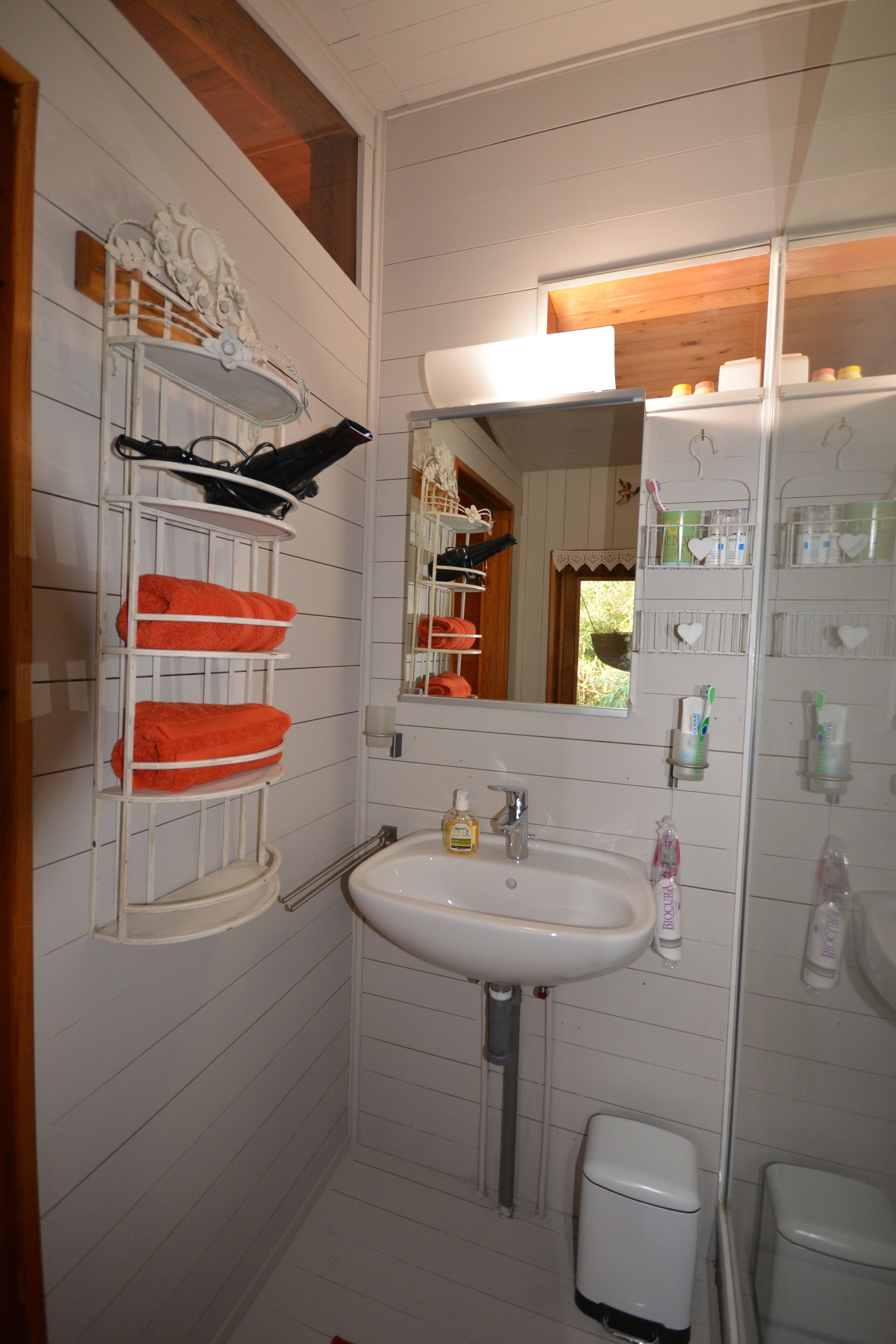 A bathroom with a white sink, a mirror, a toilet, and a shelf with orange towels.