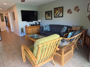 Ein Wohnzimmer mit einer Couch, zwei Korbstühlen, einem Couchtisch, einem Fernseher und Kunstwerken an der Wand.
