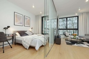 A modern bedroom with a bed, bedside table, chair, and a glass partition. - Spacious Apartment in the Center | Workspace (Warszawa)