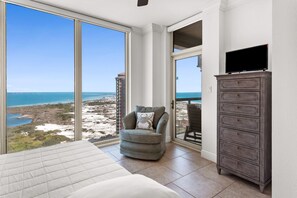 A bedroom with a large window, a chair, a dresser, and a television. - 🩴🌴Resort Amenities | Sound and Gulf Views | Private Grill | Portofino 4-1802 (Pensacola Beach)