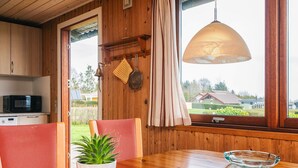 Ein Holzinterieur mit Esstisch, Stühlen, einem Blumentopf, einem Gesellschaftsspiel und einem Fenster mit Blick auf Häuser.