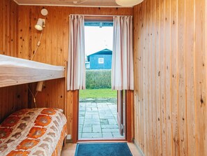Quarto de madeira com beliche, uma mesinha e janela com cortinas.