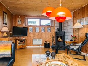 Uma sala de estar aconchegante com lareira, paredes de madeira, televisão e um espaço de estar confortável.