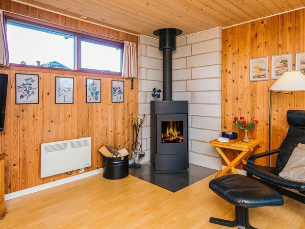 A cozy room with a wood-paneled interior, a black wood stove, a radiator, a chair, and framed botanical prints on the wall.
