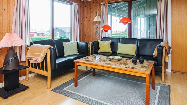 Ein Wohnzimmer mit einer Couch, einem Couchtisch, einer Lampe und großen Fenstern.