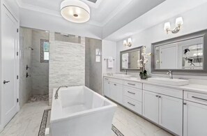 Een moderne badkamer met een vrijstaand bad, een grote spiegel en een douchehoek.