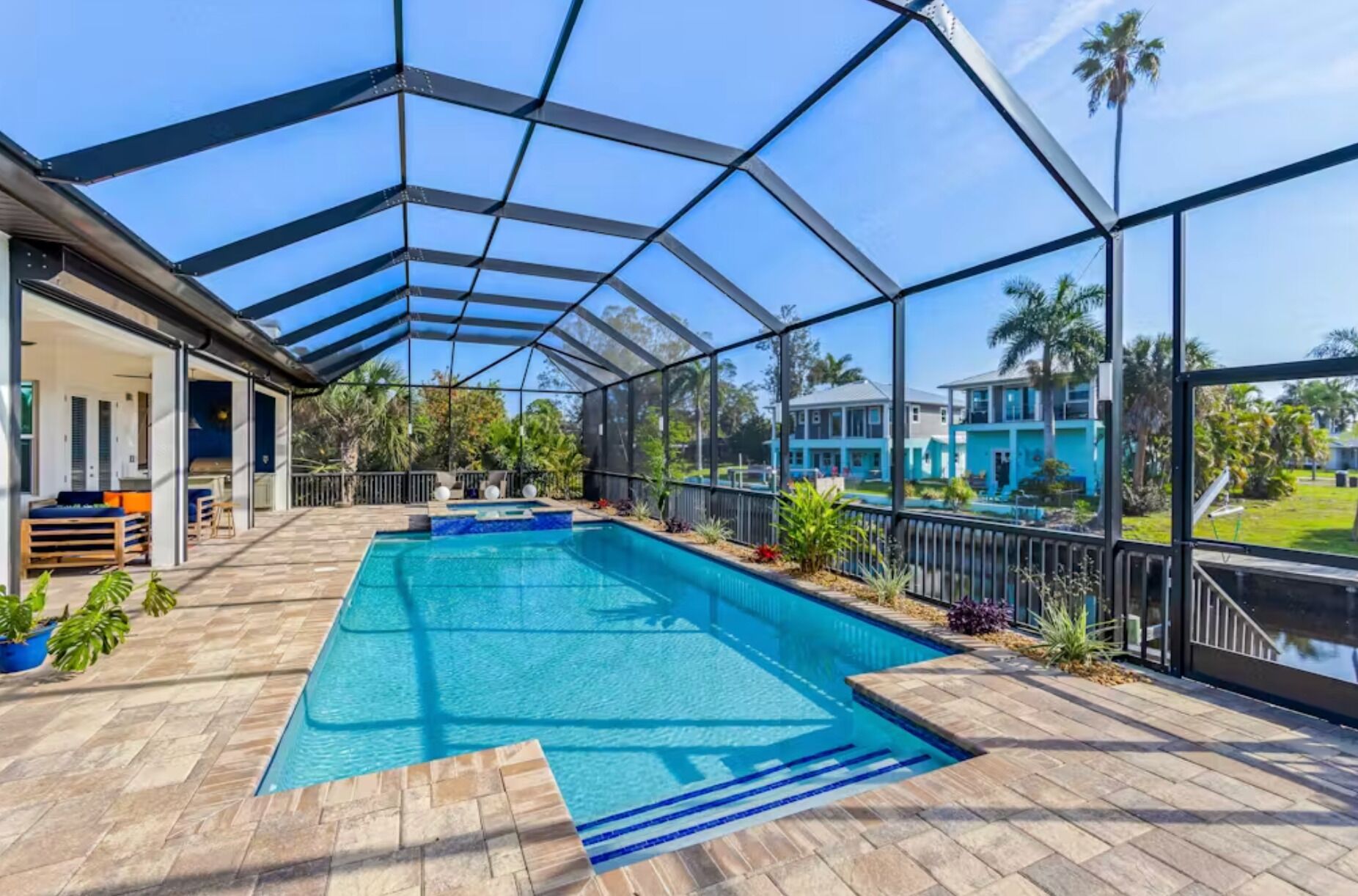 Una piscina cubierta al aire libre con zona de patio, vista a una casa azul y cielo despejado.