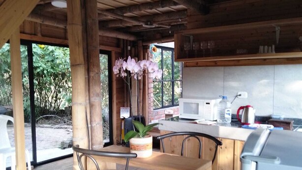Eine rustikale Küche mit Holzbalken, einem Holztisch mit zwei Hocker und einem Blumentopf, sowie einem weißen Kühlschrank.