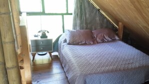 Ein Schlafzimmer mit einem Bett, zwei Kissen, einem Nachttisch mit Telefon und einem Fenster mit Vorhängen.