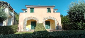 Un bâtiment à deux étages, doté d’arcs en pierre, de volets verts et surplombant un ciel dégagé.