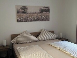 A bedroom with a bed, two pillows, a bedside table, a lamp, and a wall-mounted picture. - Holiday apartment Lindenplatz in our guesthouse in old town of Zell (Moselle) (Zell (Mosel))