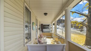 Een overdekte veranda met een bank, een tafel en uitzicht op een besneeuwd landschap met bomen.
