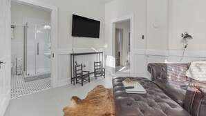 Een moderne slaapkamer met een douchecabine van glas, een flatscreen-tv, een leren bank en een ruw vloerkleed.